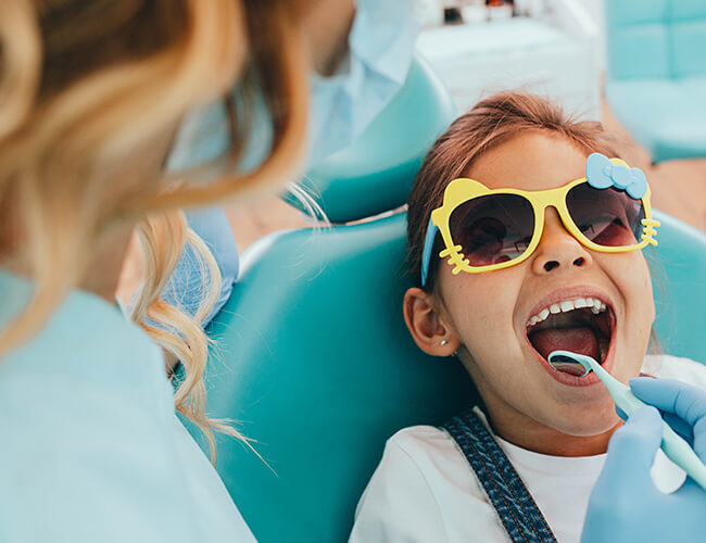 A child wearing glasses while she's being examined by her dentist