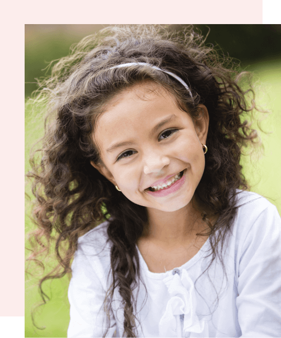 A young girl with curly hair is smiling outdoors